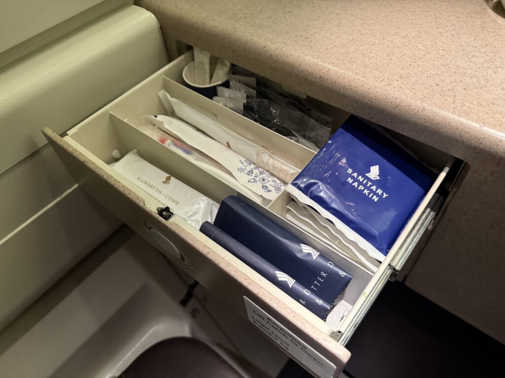 Airplane bathroom drawer filled with: dental kits, sanitary napkins, combs, mini lotions and wipes.